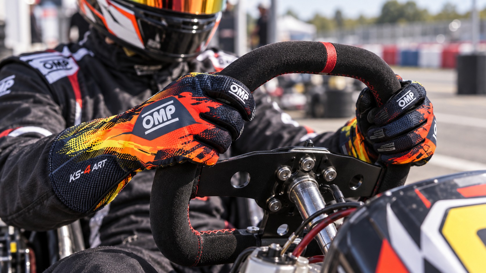 Kart driver wearing black, orange and yellow OMP KS-4 Art gloves on an outdoor kart circuit