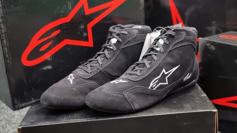 A pair of black Alpinestars SP V2 race boots sitting on their box in front of Alpinestars boxes in the GSM Performance showroom