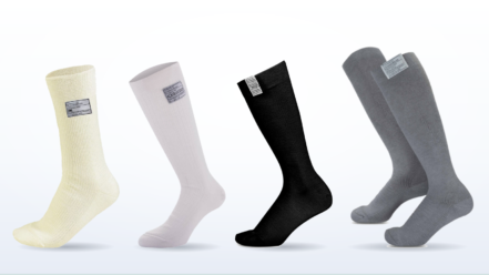 Four FIA 8856-2018 fire resistant motorsport socks side by side, left to right the OMP First calf length sock in cream, the Alpinestars Race V4, the Sparco Nomex calf sock and the knee length Walero 2.0