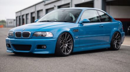A blue BMW E46 M3 coupe lowered on coilovers, parked in a circuit pit lane