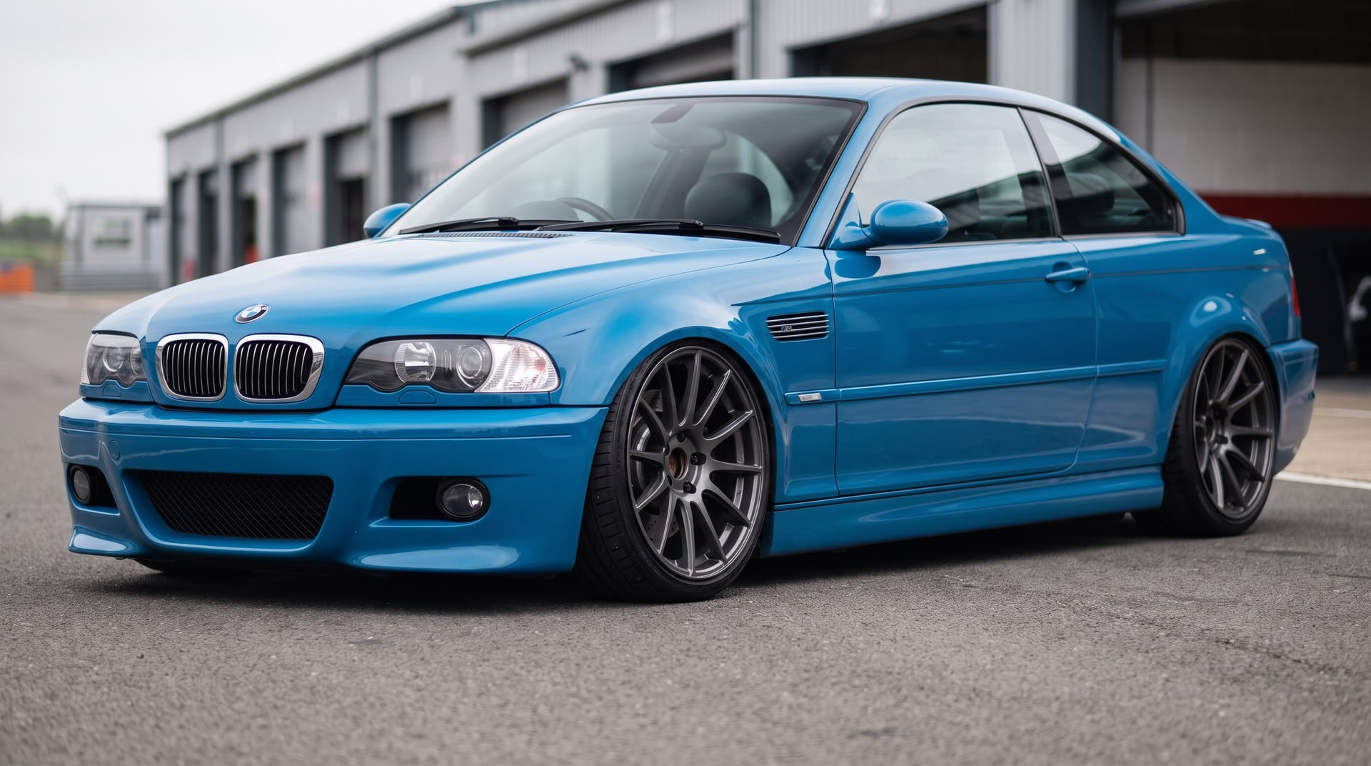 A blue BMW E46 M3 coupe lowered on coilovers, parked in a circuit pit lane