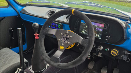 The interior of a customer's blue Ford Escort with a suede OMP steering wheel on a gold quick release, a digital dash and a switch panel