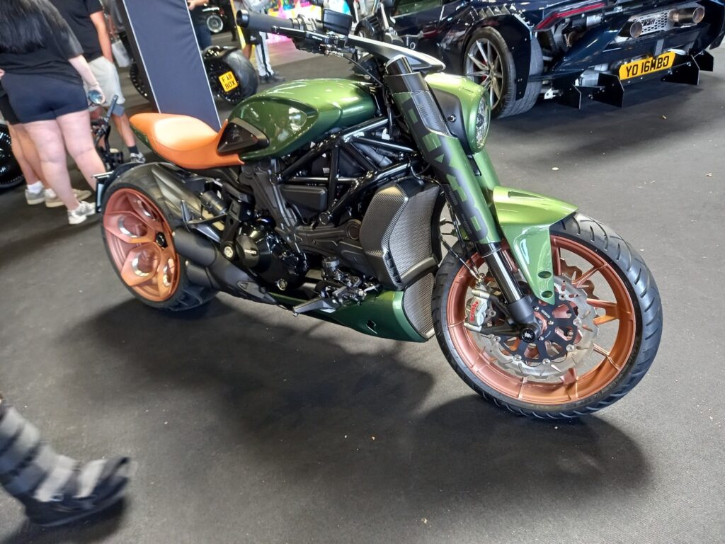 Ducati Diavel V4 in metallic green with copper wheels and a tan seat, a Lamborghini behind