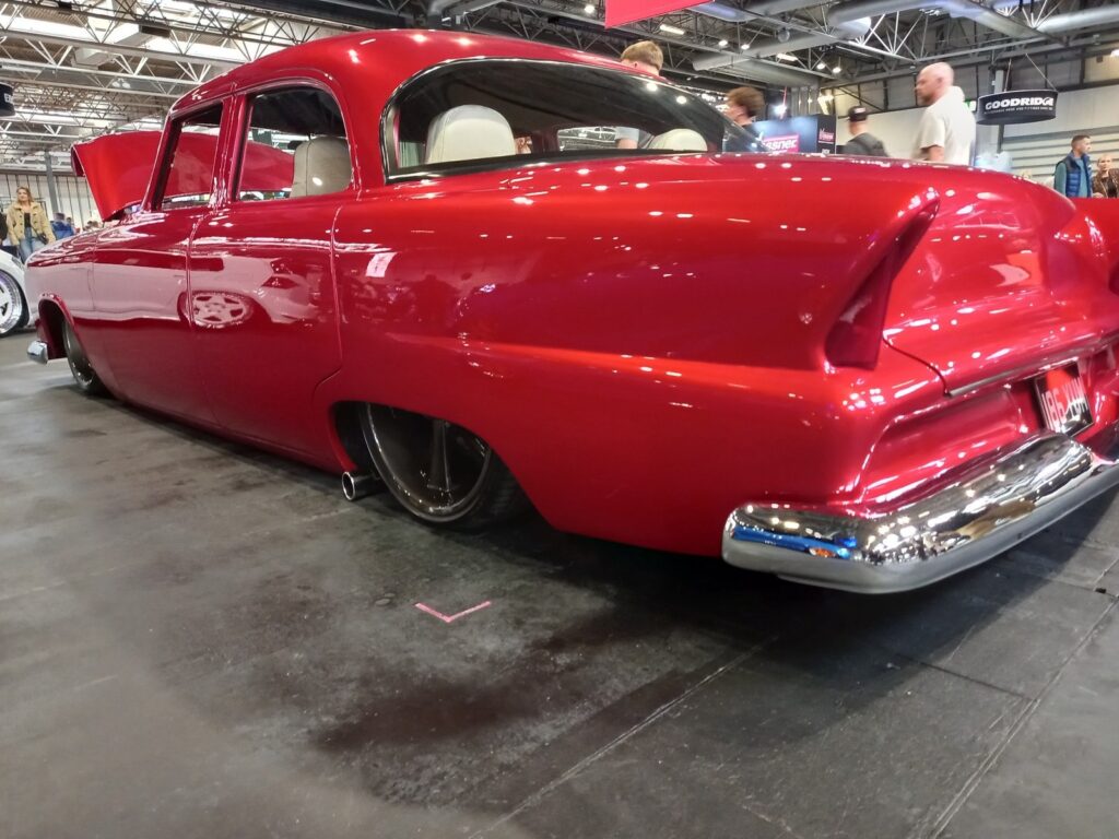 Candy red 1950s American sedan with tail fins, sitting on the floor on air ride, rear three quarter view