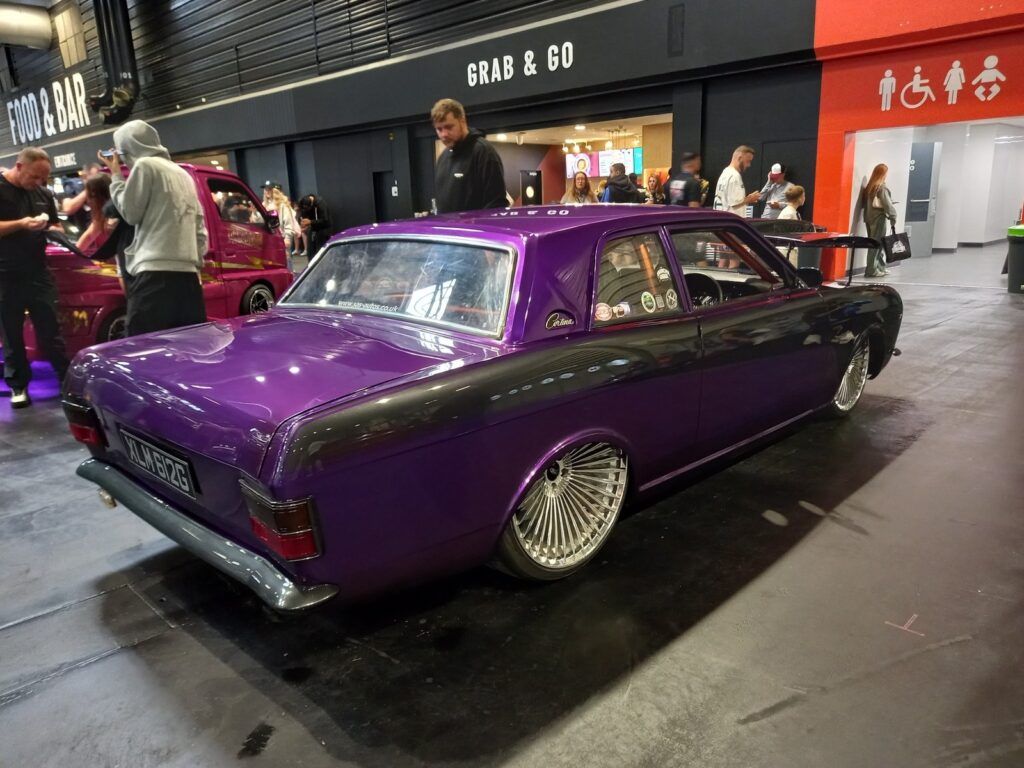 Purple Ford Cortina Mk2 two door on turbine style wheels, sitting on the floor on air ride, outside the food hall