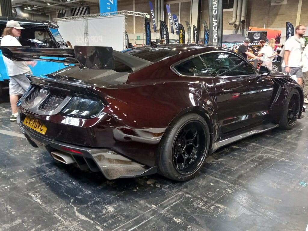 Black cherry Ford Mustang S650 with a carbon wide-body kit and a tall rear wing, rear three quarter view