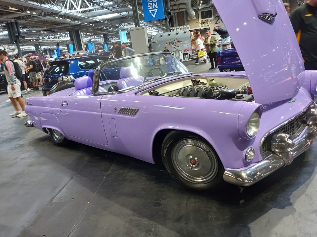 Lilac 1950s Ford Thunderbird convertible with its bonnet up showing a modern V8, on steel wheels with chrome hubcaps