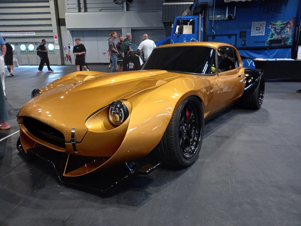 Gold wide-arch Jaguar E-Type restomod with black multi-spoke wheels, red calipers and a deep front splitter