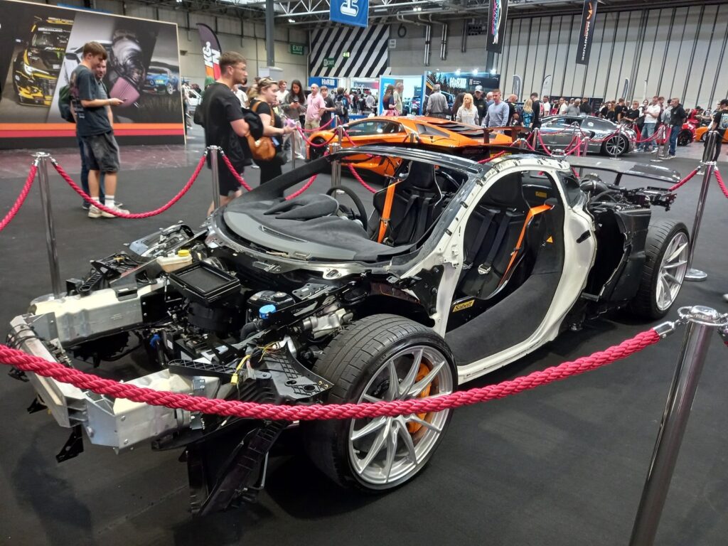 A McLaren stripped to its bare carbon tub and running gear, with orange calipers, on display at Gravity Show 2026