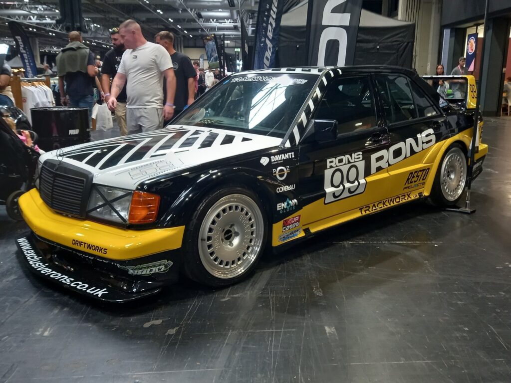 Mercedes 190E Evolution II in a black, white and yellow DTM style livery, number 99, with Corbeau and JP Cages logos on the sill