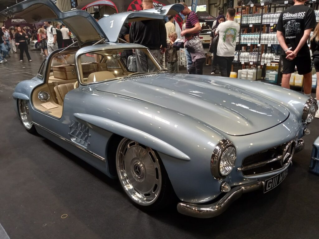 Light blue Mercedes 300SL Gullwing from the front with doors up and polished disc wheels, Gravity Show 2026