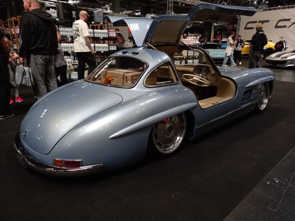 Light blue Mercedes 300SL Gullwing with both doors raised and a cream interior, rear three quarter view
