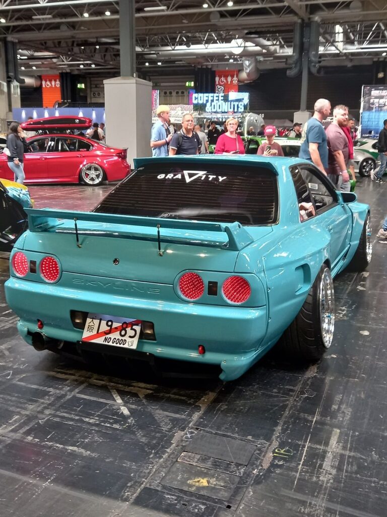 Teal wide-arch Nissan Skyline R32 with a Gravity rear screen decal and a large rear wing, from behind