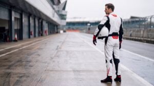 Racing driver in Alpinestars GP Tech V4 white black and red race suit standing in a British circuit pit lane