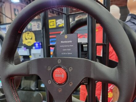 A MOMO Montecarlo leather steering wheel with a red horn button on a MOMO display stand