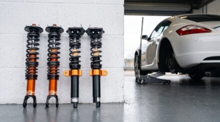 A MOTON 1-way Clubracer kit stood against a pit garage wall with a Porsche Cayman on a jack