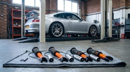 A MOTON 2-way coilover kit on a moving blanket in a race workshop with a Porsche 911 GT3 on a lift