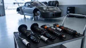 A MOTON 3-way coilover kit on a trolley in a pit garage with a GT race car on stands behind