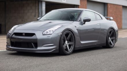 A grey Nissan GT-R R35 lowered on coilovers, parked in a circuit paddock