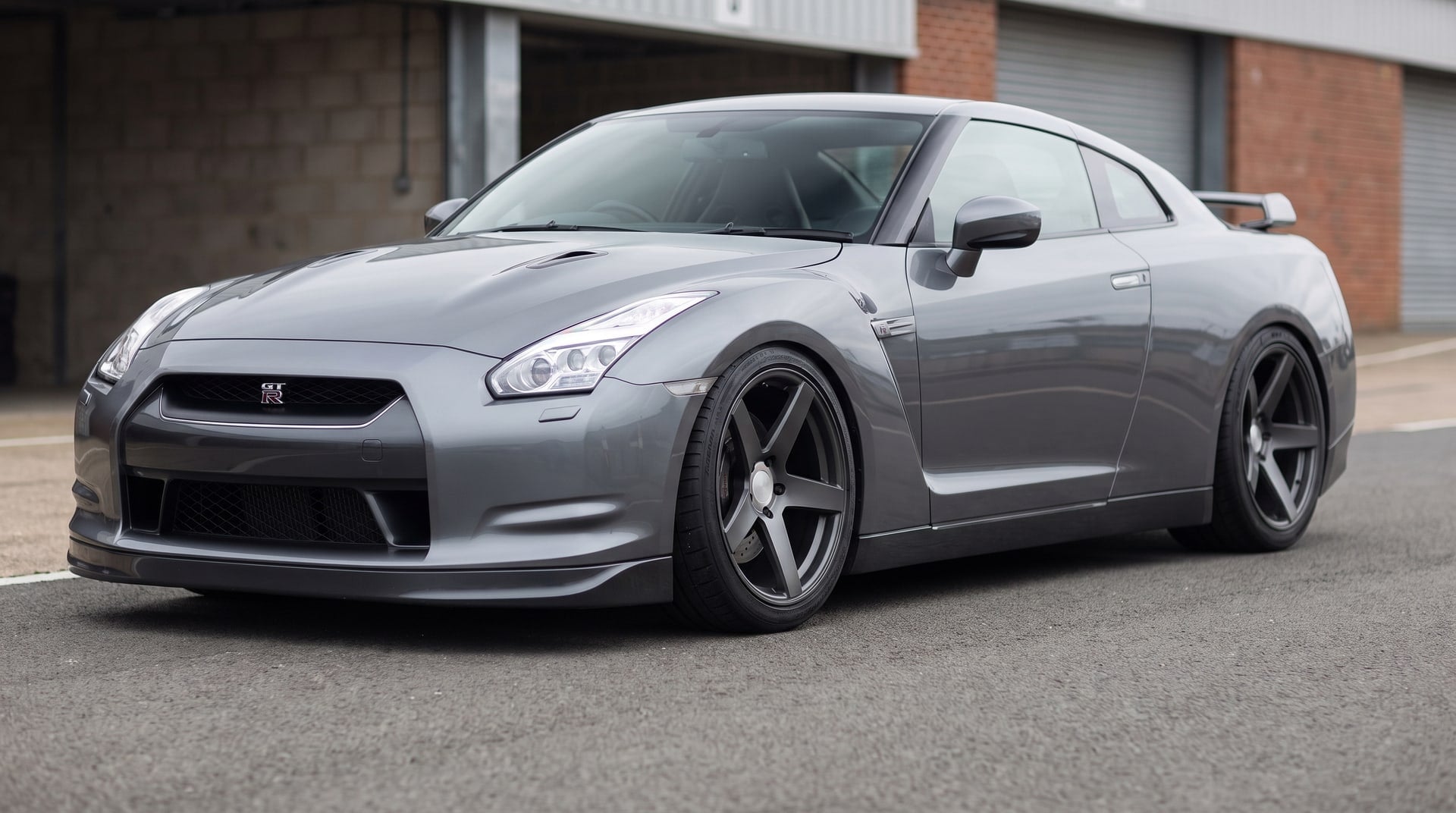 A grey Nissan GT-R R35 lowered on coilovers, parked in a circuit paddock