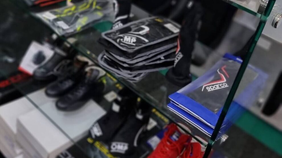 Racing gloves in OMP and blue Sparco packets with race boots on the glass shelves of the GSM Performance showroom