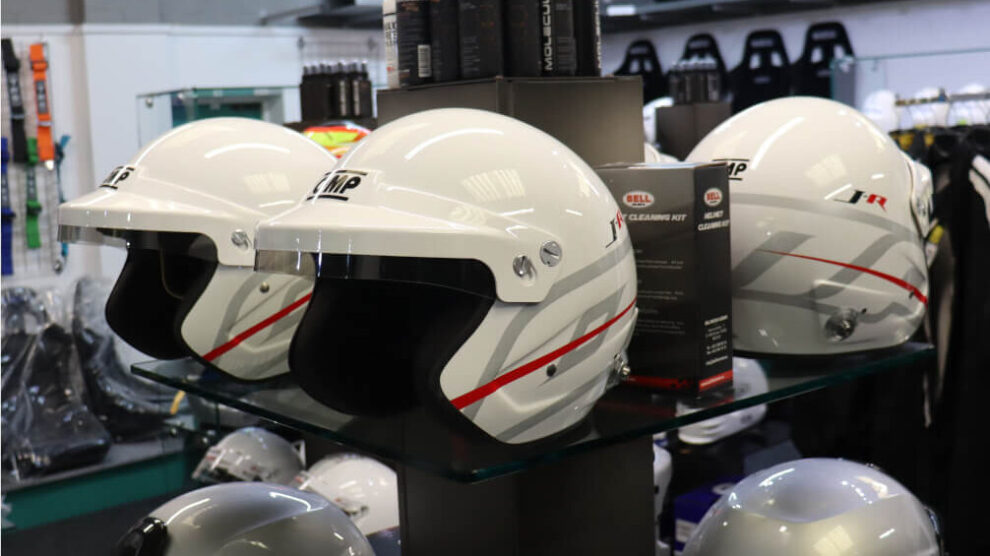 White OMP J-R open face helmets with red and grey stripes on a glass display stand in the GSM Performance showroom
