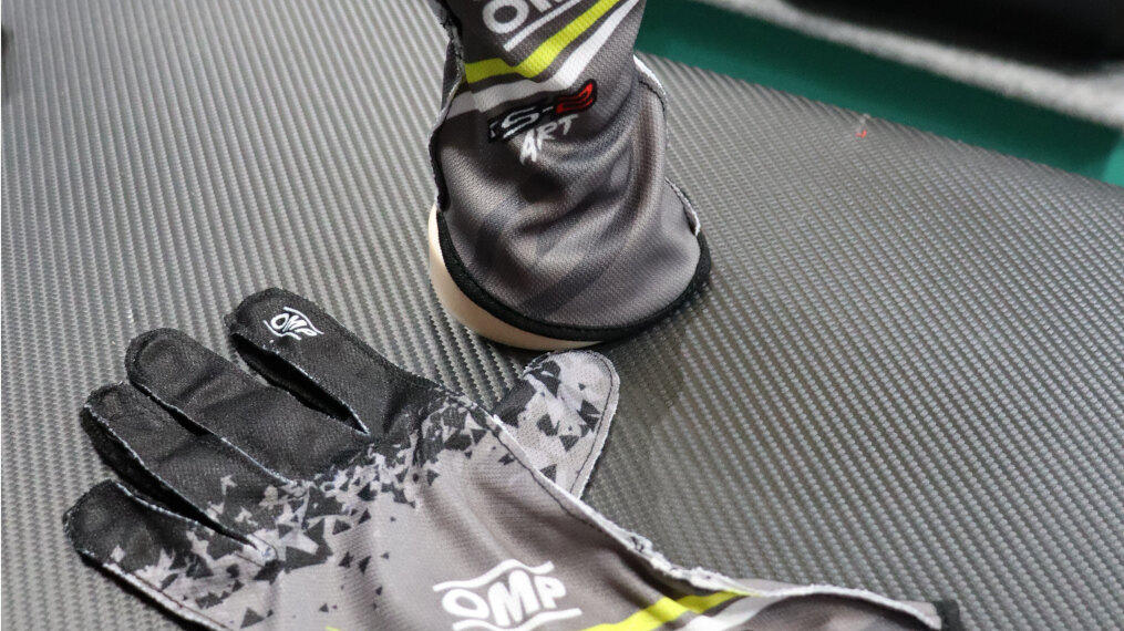 A pair of anthracite OMP KS-2 Art kart gloves on a carbon-effect counter in the GSM Performance showroom
