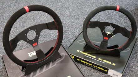 Two OMP Red Edition suede steering wheels with red stitching on stands on top of their OMP boxes