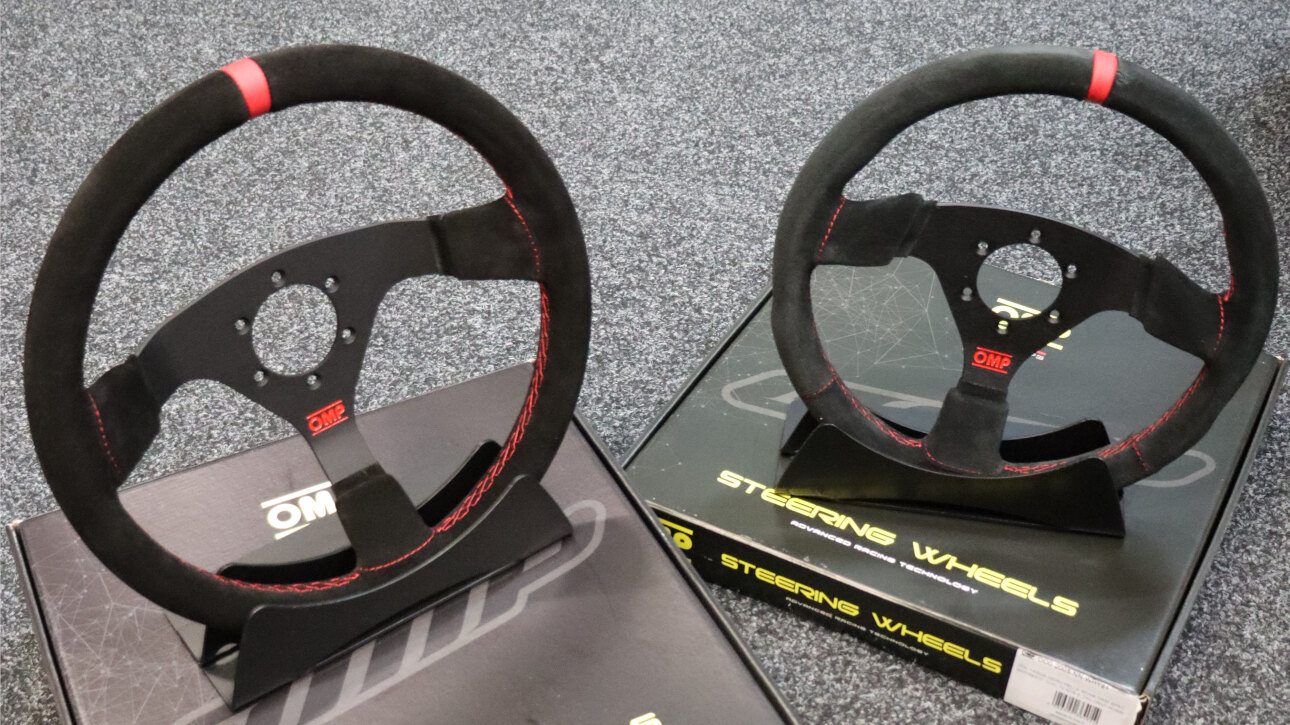 Two OMP Red Edition suede steering wheels with red stitching on stands on top of their OMP boxes