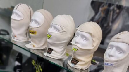 A row of fireproof racing balaclavas from several brands on a glass shelf in the GSM Performance showroom