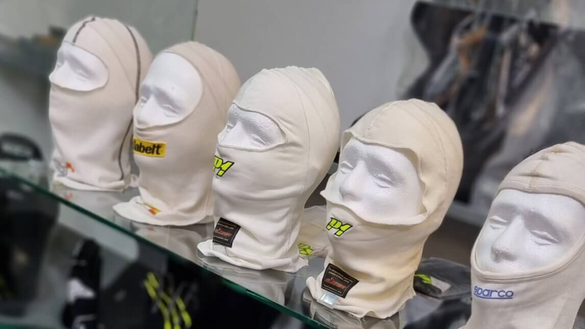 A row of fireproof racing balaclavas from several brands on a glass shelf in the GSM Performance showroom