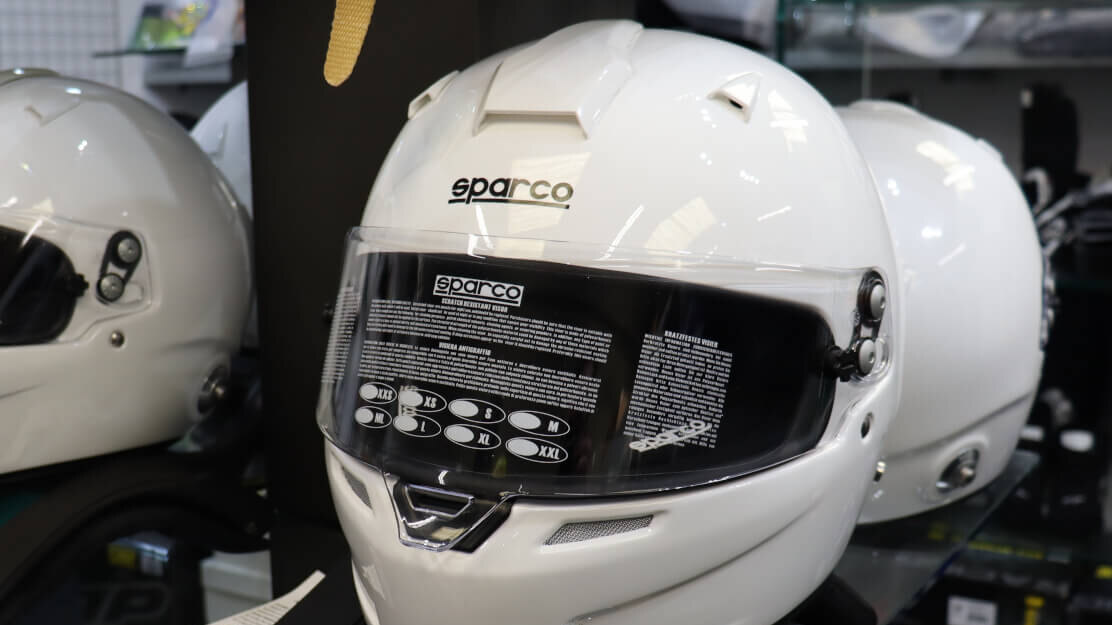 A white Sparco full face helmet on a stand among other helmets in the GSM Performance showroom
