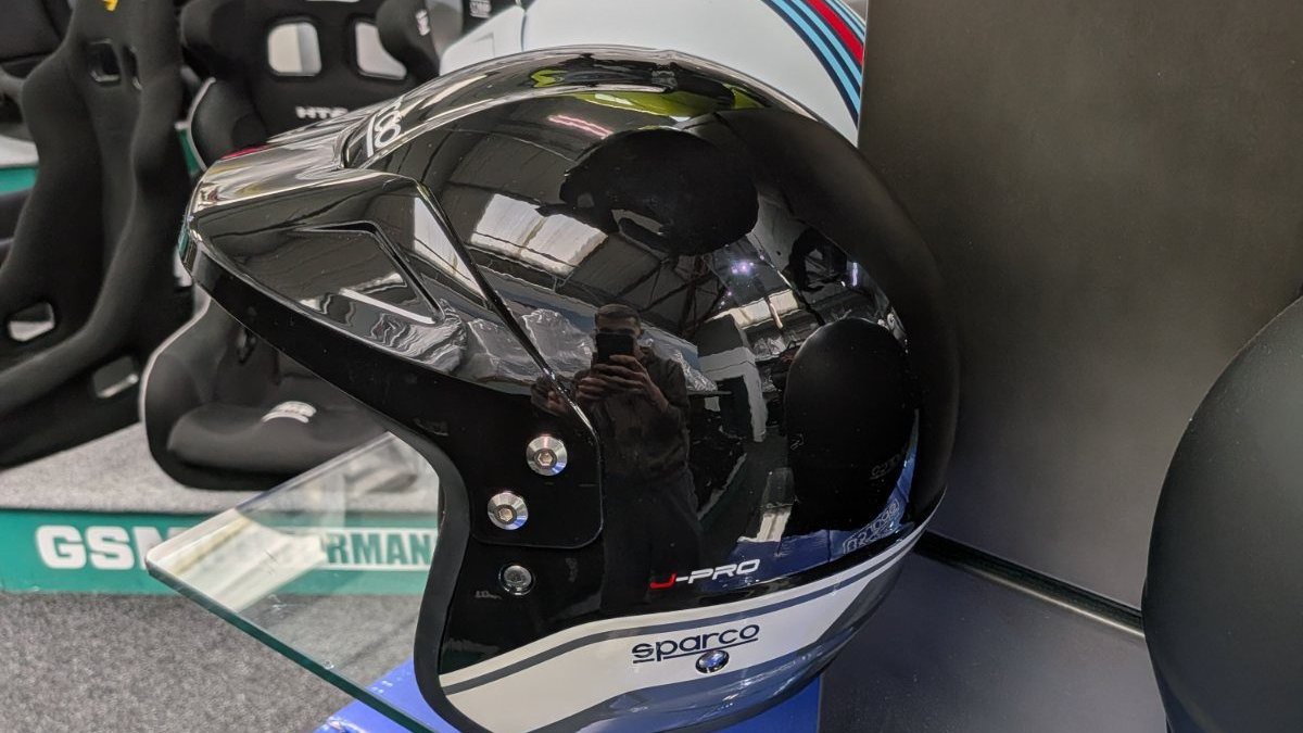 The black and grey Sparco J-Pro on the glass shelf in the GSM Performance showroom, with the J-PRO and sparco marks on the white band clearly visible and bucket seats behind