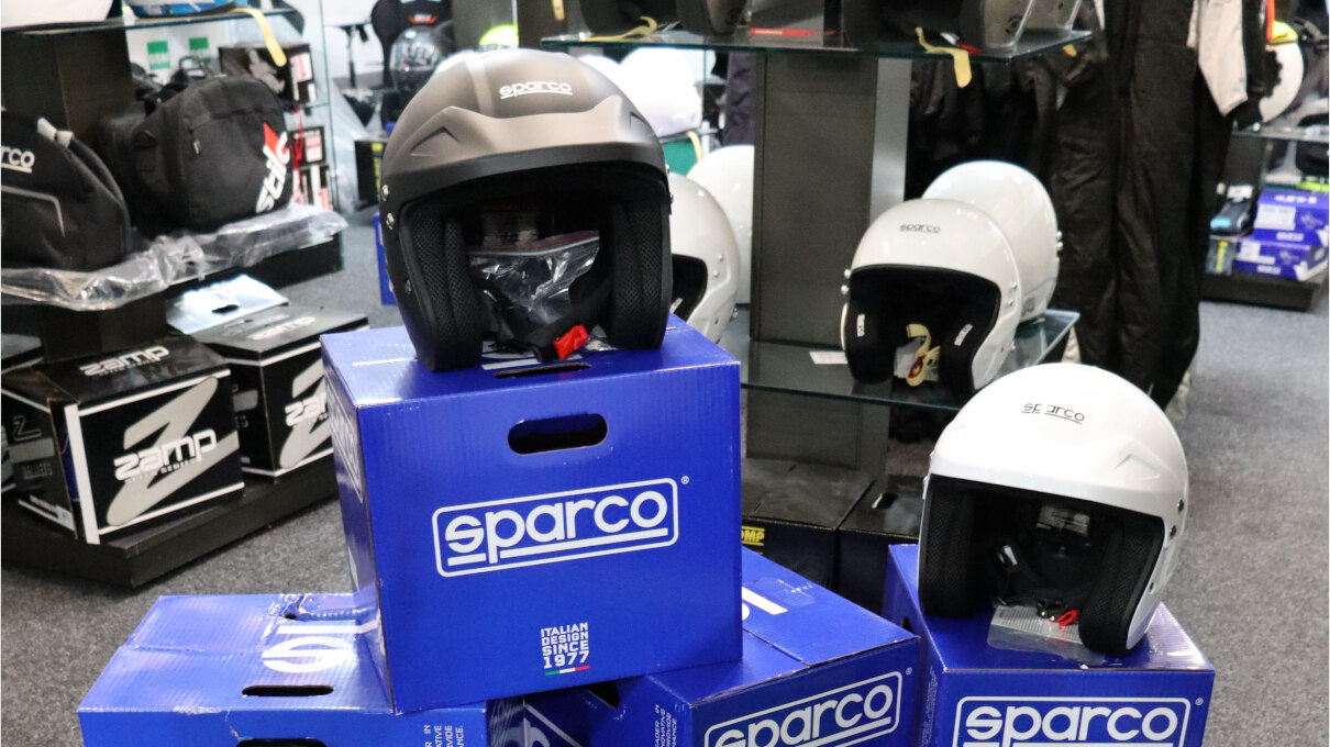 Matt black and white Sparco J-Pro open face helmets on stacked blue Sparco boxes in the GSM Performance showroom