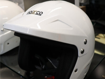 A white Sparco J-Pro open face helmet on a glass shelf in the GSM Performance showroom