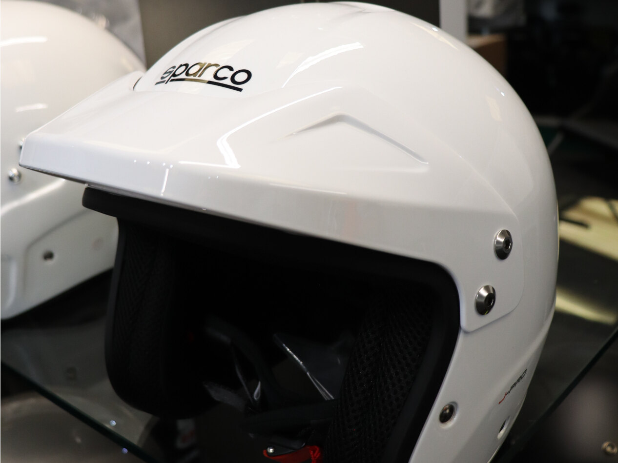 A white Sparco J-Pro open face helmet on a glass shelf in the GSM Performance showroom