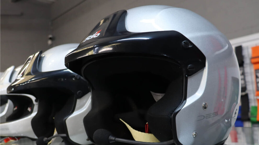 Silver Stilo open face rally helmets with intercom microphones on a glass shelf in the GSM Performance showroom