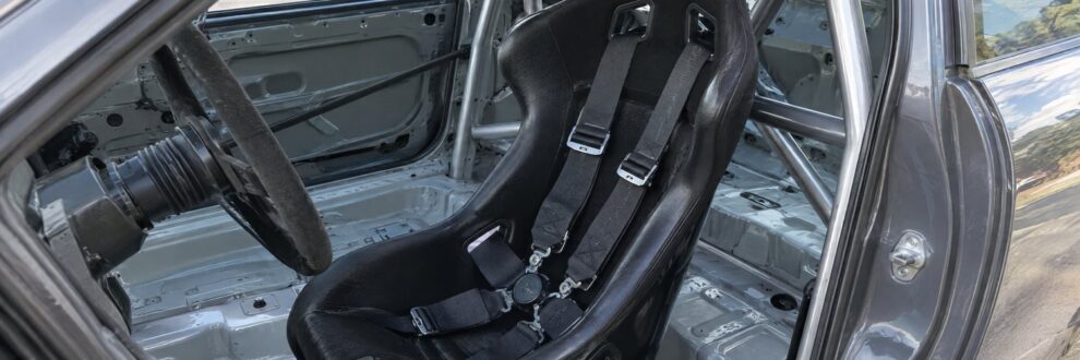 A black bucket seat and harness in a stripped race car interior
