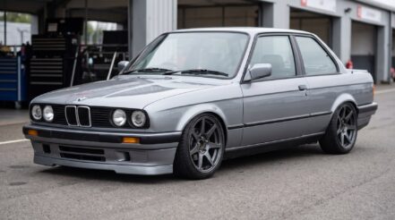 BMW E30 3 Series on coilovers in the pit lane, silver grey body, dark alloy wheels, low stance