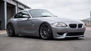 A BMW Z4 M Coupe in silver grey, sitting low on coilovers in a pit lane, dark aftermarket wheels with open hubs