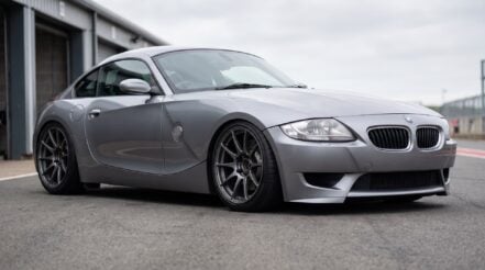 A BMW Z4 M Coupe in silver grey, sitting low on coilovers in a pit lane, dark aftermarket wheels with open hubs
