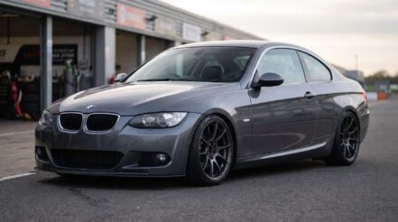 BMW E92 3 Series coupe on coilovers in a pit lane: arch gap closed, dark aftermarket wheels, a little camber