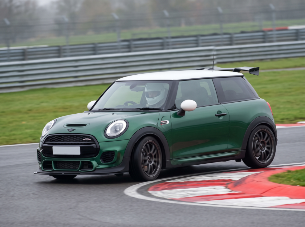 2019 MINI John Cooper Works in British Racing Green at a British race circuit apex, helmeted driver visible at the wheel, red and white kerbing