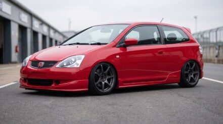 A Honda Civic EP3 Type-R sat low on coilovers, arch gap closed at both ends, a touch of camber at the front, dark aftermarket wheels in a pit lane