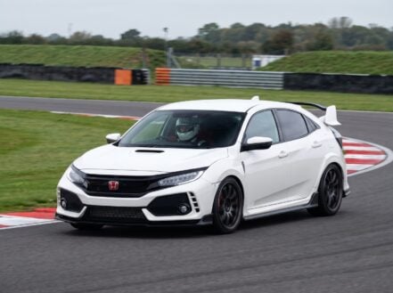 White Honda Civic Type R FK8 cornering on a British race circuit, helmeted driver visible through the windscreen in a white full-face helmet