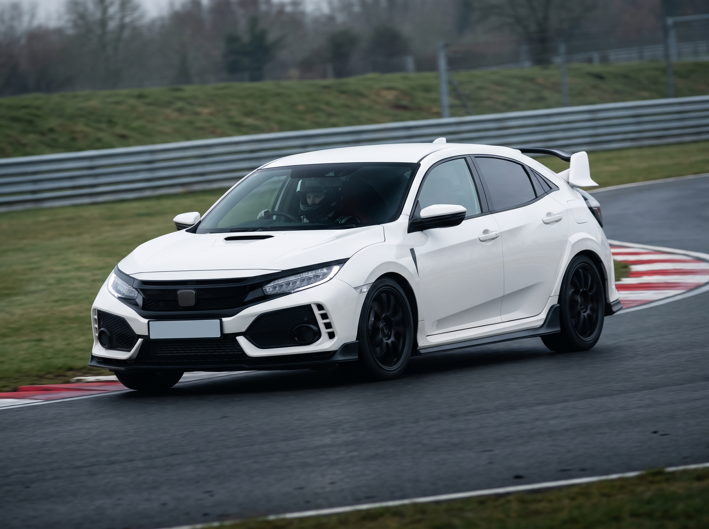 White Honda Civic Type R at a British race circuit apex with helmeted driver visible through the windscreen, red and white kerbing, overcast trackday light